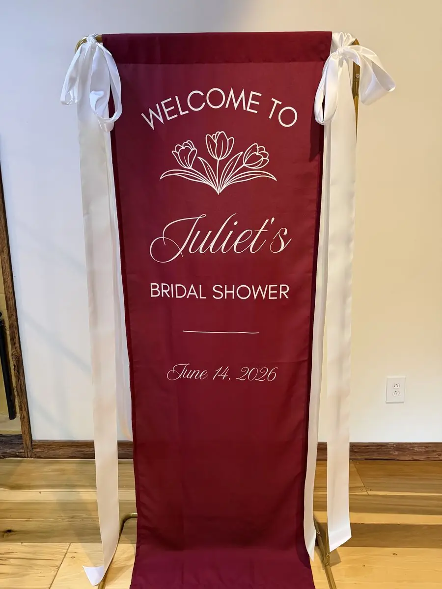 Deep burgundy printed fabric banner welcoming guests to Juliet's bridal shower, finished with long white ribbon ties