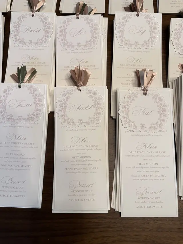 A stack of printed wedding menus with illustrated floral crests and paper tassels