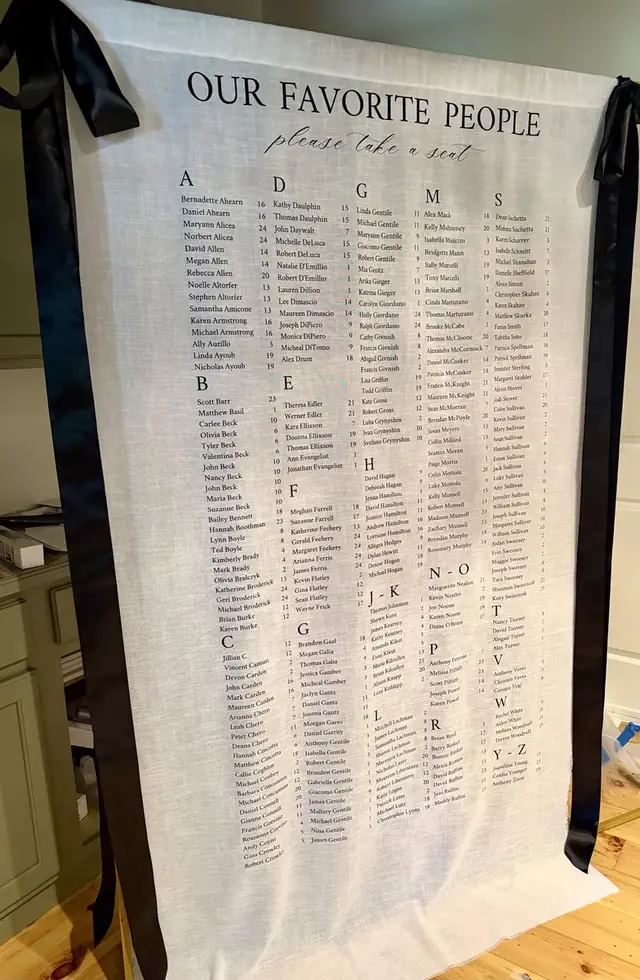 Fabric seating chart titled Our Favorite People with black ribbon ties, hung against a panelled wall