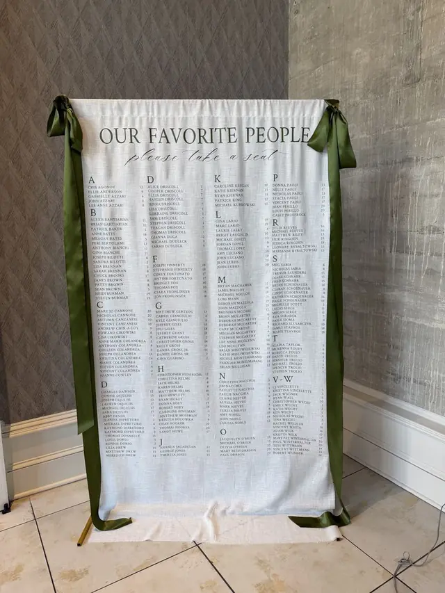 Fabric seating chart banner titled Our Favorite People with guest names in columns and olive green ribbon ties